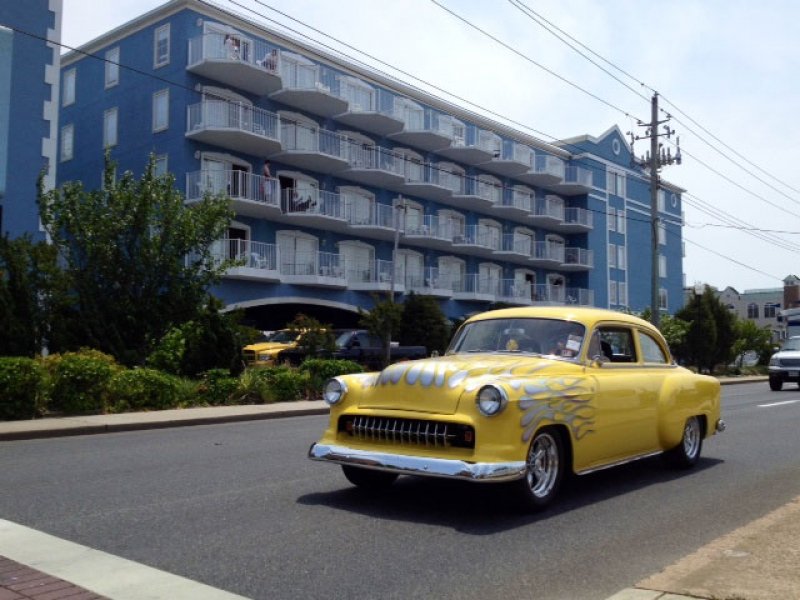 an old yellow car driving down the street